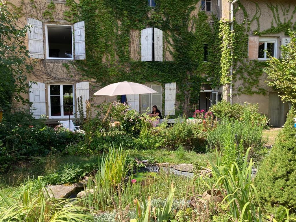 una persona sentada bajo una sombrilla en un jardín en Chambres d'hôtes proche d'Epinal, Vosges 88270, 