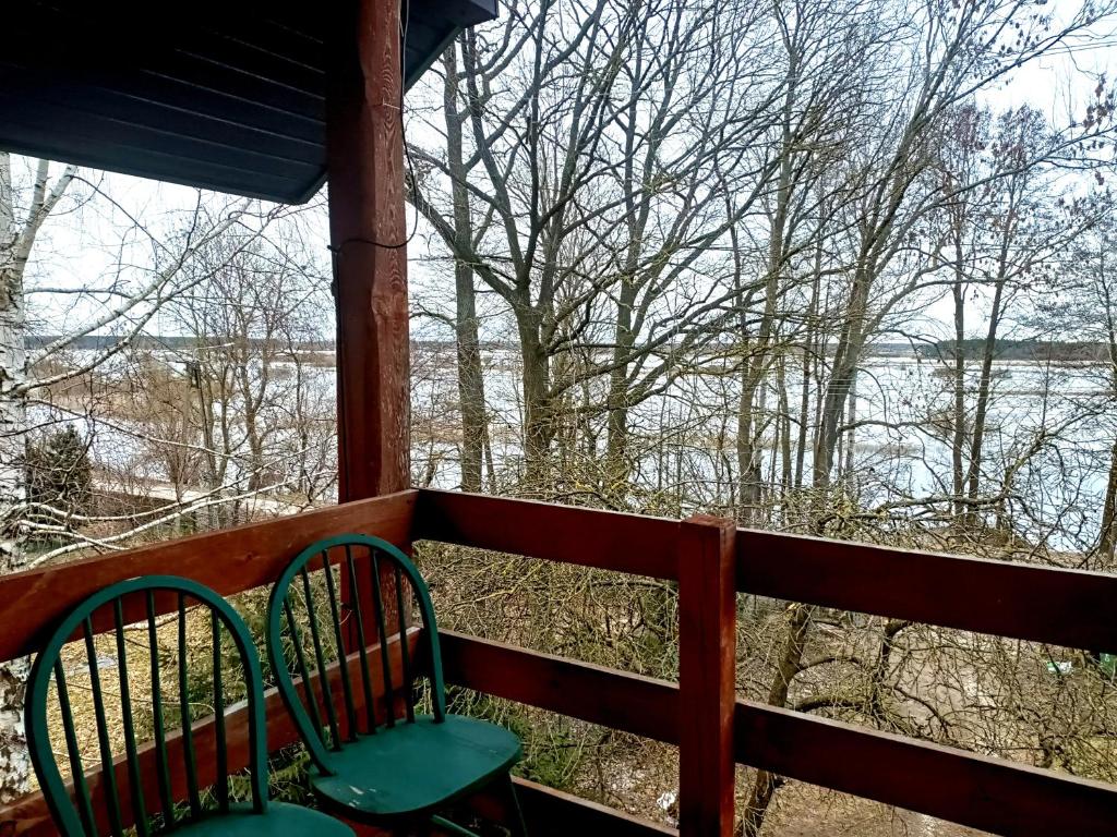2 Stühle auf einer Veranda mit Blick auf das Wasser in der Unterkunft Kalinówka - apartament w domu nad Narwią in Wizna