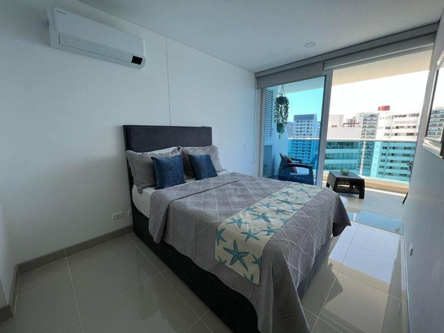 Un dormitorio con una cama con almohadas azules y una ventana en apartamento con vista al mar, en Santa Marta