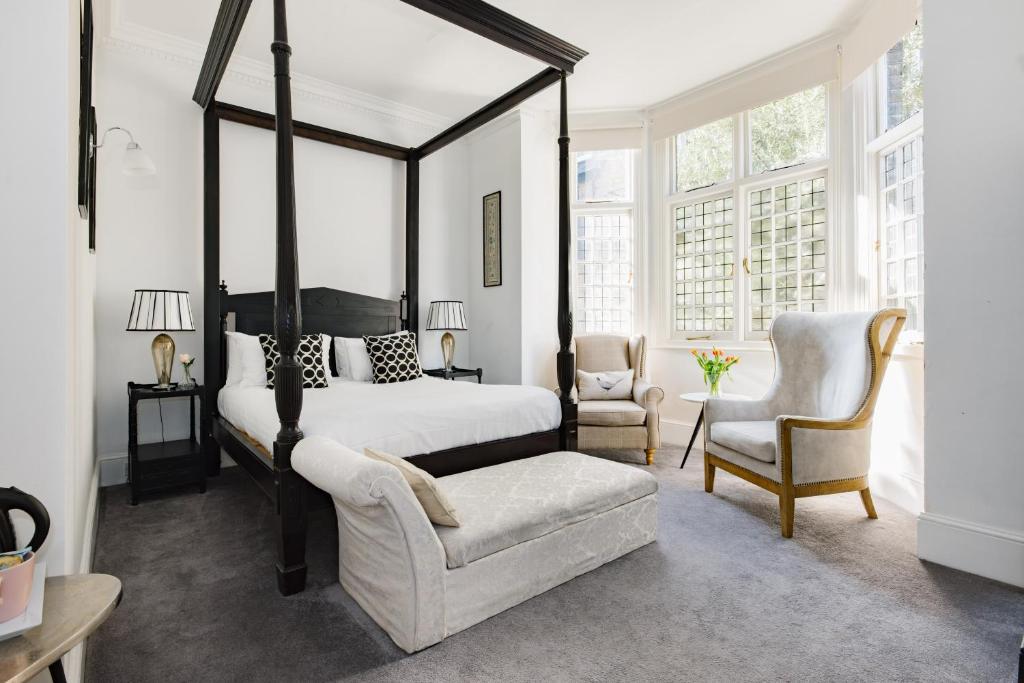 um quarto com uma cama de dossel e uma cadeira em The Abbey Notting Hill em Londres