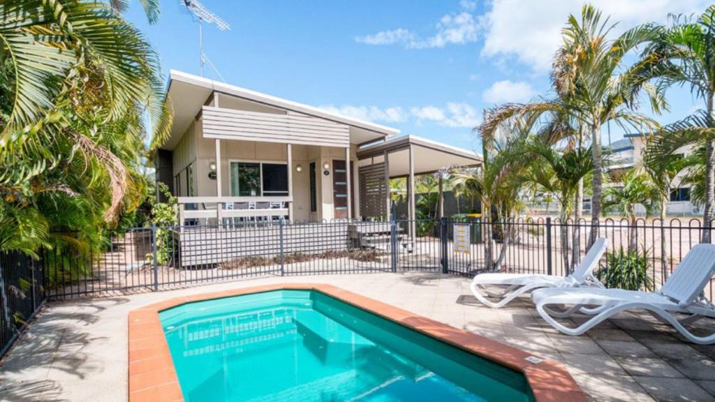 a swimming pool in front of a house with two chairs at Dolphin Escape Holiday House in Horseshoe Bay