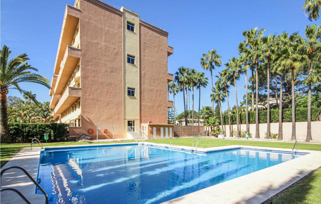 マルベーリャにあるStunning Apartment In Las Chapas With 1 Bedrooms, Wifi And Outdoor Swimming Poolのヤシの木が茂る建物の前にあるスイミングプール