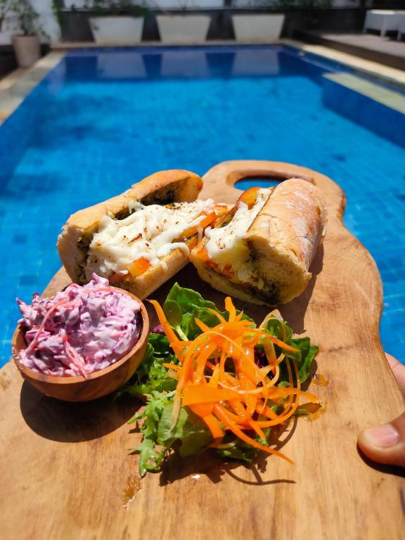 a wooden cutting board with a sandwich and a salad at Bale Sampan Boutique Bungalows in Gili Trawangan