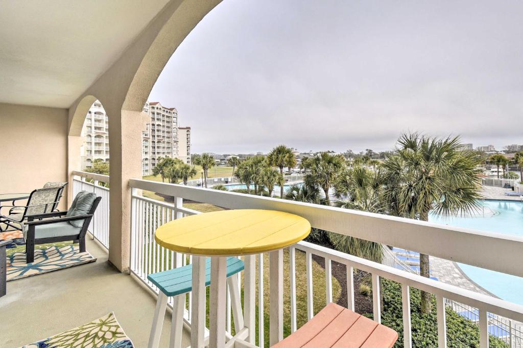 a balcony with a yellow table and chairs and a pool at Barefoot Resort Condo with Balcony and Pool Views! in Myrtle Beach