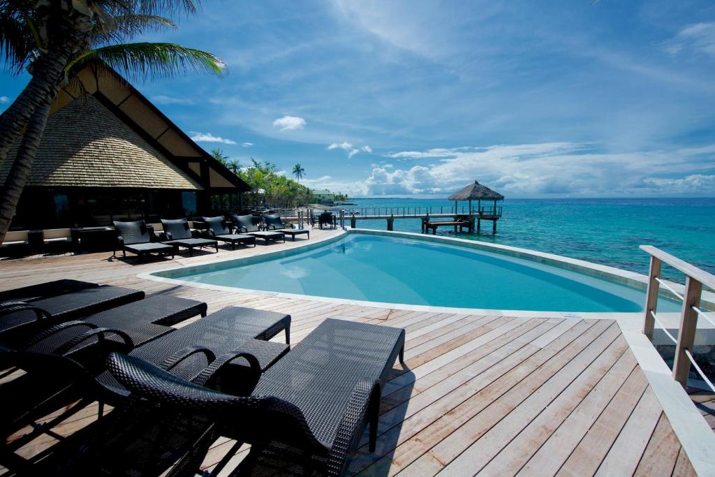 a swimming pool with chairs and the ocean in the background at Maitai Rangiroa in Avatoru