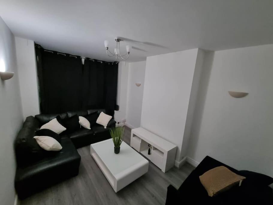 a living room with a black couch and a white table at A Beautiful Premium 4-Bedroom House With Parking (Reading West) in Reading