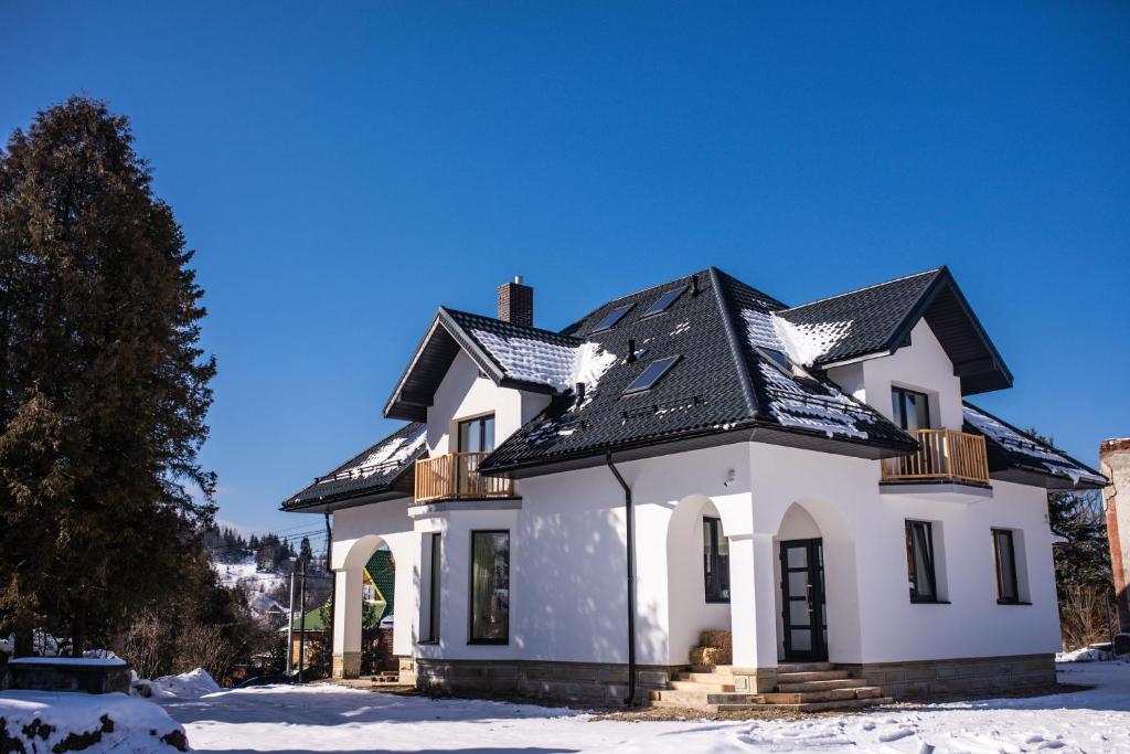 a white house with a black roof in the snow at Grand Villla Skyta in Vorokhta