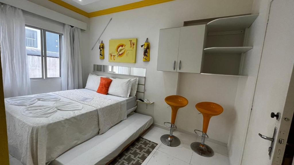 a small bedroom with a bed and two stools at Pousada Águas do Mariscal in Bombinhas