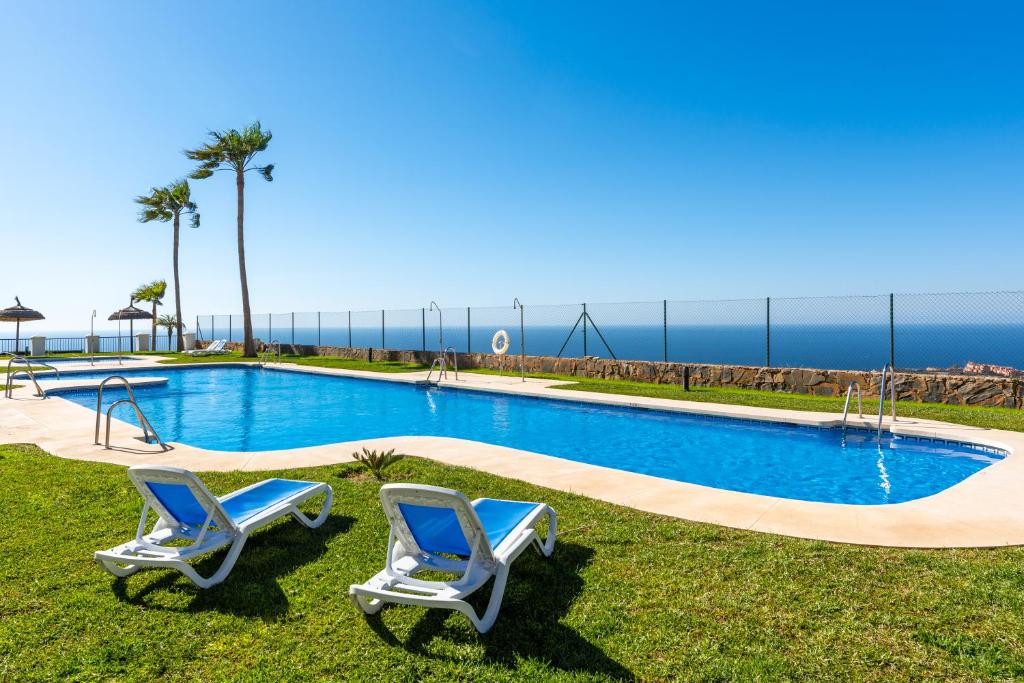 a pool with two chairs and the ocean in the background at Ceres Luxury Apartment in Rincón de la Victoria