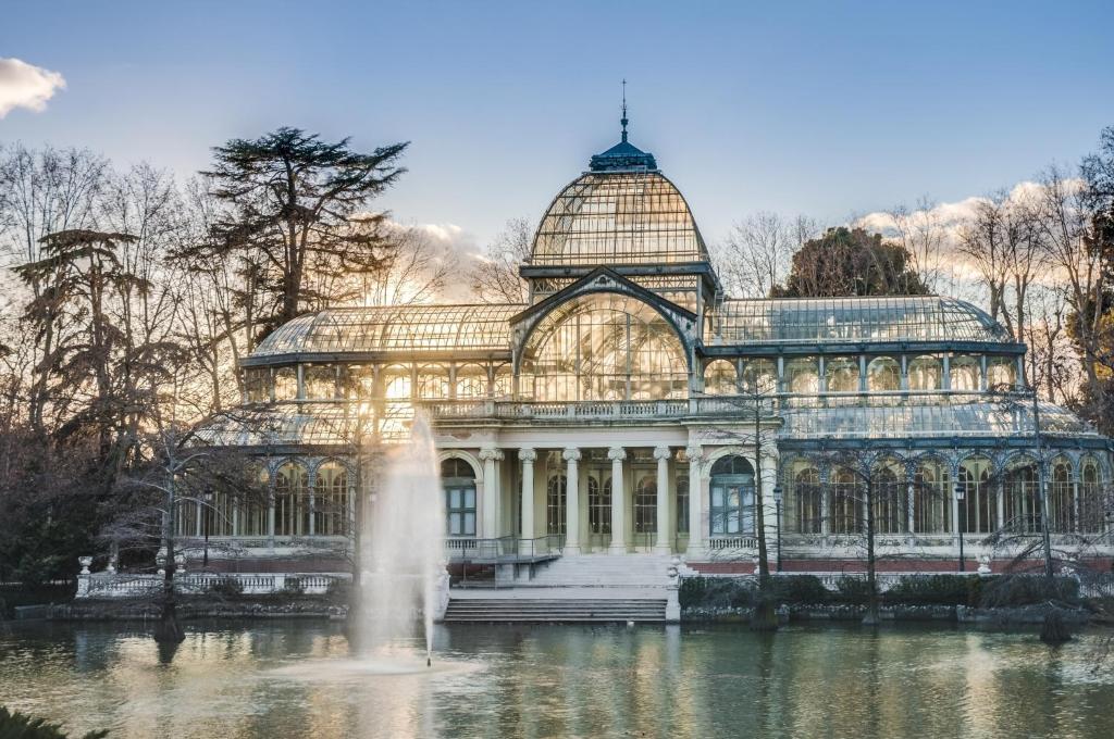 a large glass house in a pond with a fountain at De El Retiro al cielo in Madrid