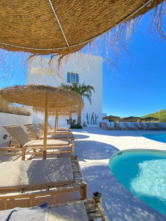 un resort con piscina, sedie e ombrellone di paglia di The Olive Boutique Suites & Spa a Cala Llonga