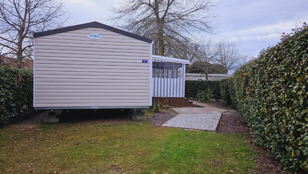 a large white shed in a yard next to a hedge at Joli Mobil home N°11, 4ch tout confort et spacieux in Gastes