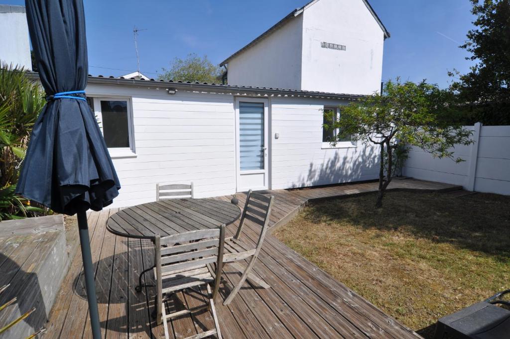 a table and chair on a deck with an umbrella at Petite maison cosy-9mn à pied gare, 5 mn plage ! in Pornichet