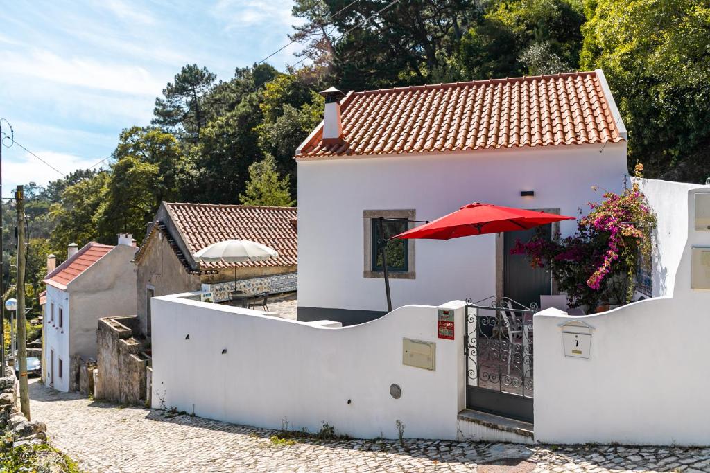 Uma casa branca com um guarda-chuva vermelho à frente. em Casota - Lusitália Eden em Sintra