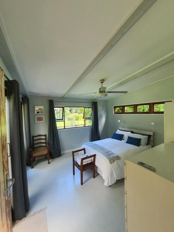 a bedroom with a bed and a chair and windows at Beautiful garden cottage in Stormsrivier