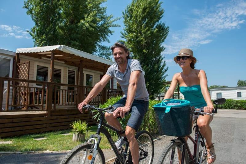 un homme et une femme faisant du vélo devant une cabine dans l'établissement Camping Officiel Siblu La Carabasse, à Vias