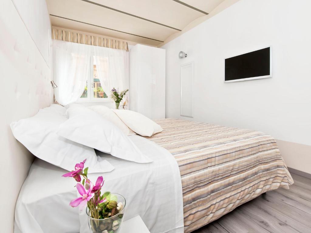 Dormitorio blanco con cama con sábanas blancas y flores púrpuras en White Rooms Colosseo, en Roma