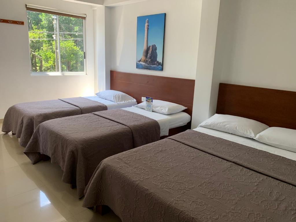 three beds in a hotel room with a window at Hotel El Faro Buga in Buga