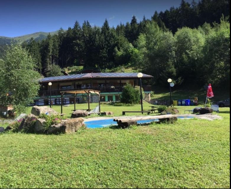 a building with a swimming pool in a field at Camping & Chalet Pian della Regina in Cevo