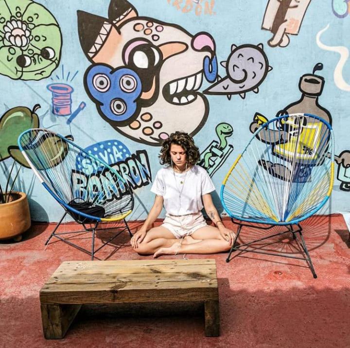 a woman sitting in front of a wall with two chairs at Gente de Más Hostel in Puebla