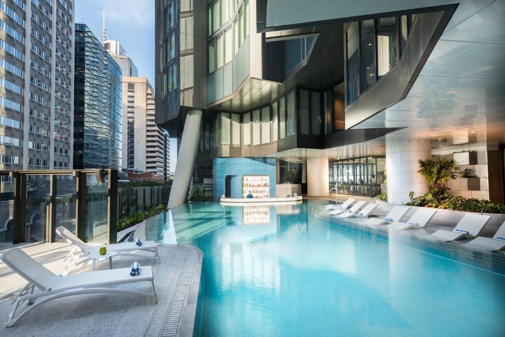 una piscina con sillas blancas y un edificio en The Westin Brisbane, en Brisbane