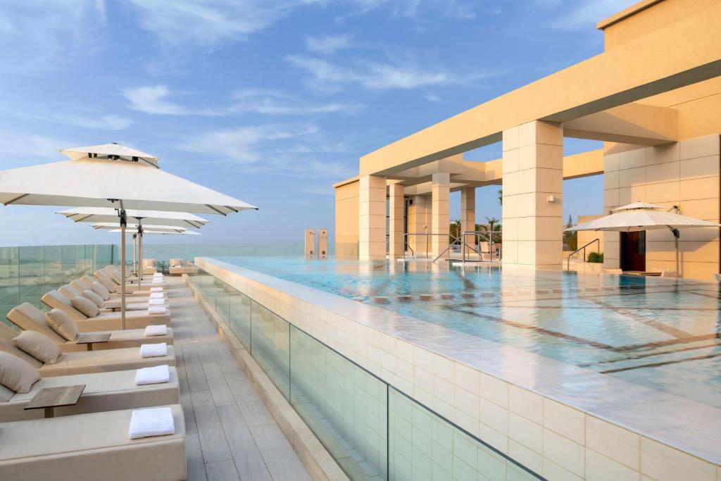 a pool with chairs and umbrellas next to a building at Agora, Doha, Autograph Collection in Doha