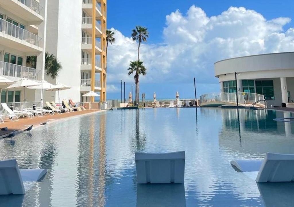 a swimming pool with chairs and a building and palm trees at Peninsula Island Resort & Spa - Beachfront Property at South Padre Island in South Padre Island