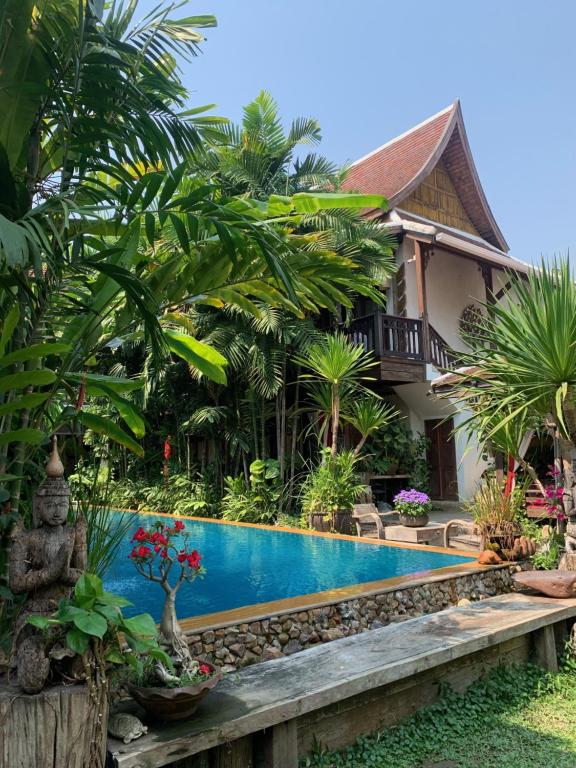 A blue pool is framed by palms, ornamental plants and a traditional villa.