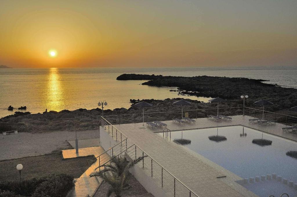 a sunset over the ocean with a swimming pool at Nanakis Beach Apartments in Stavros
