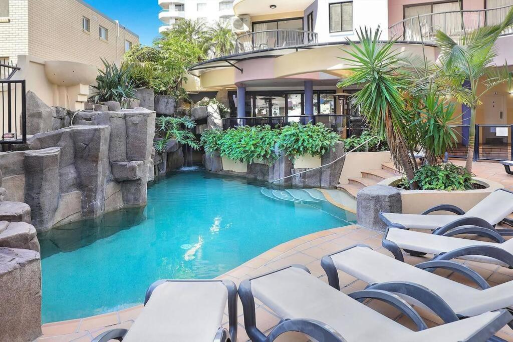 a swimming pool with chairs in front of a building at 2 Bedroom Central Mooloolaba Resort with Pool, Spa, Mini Golf in Mooloolaba