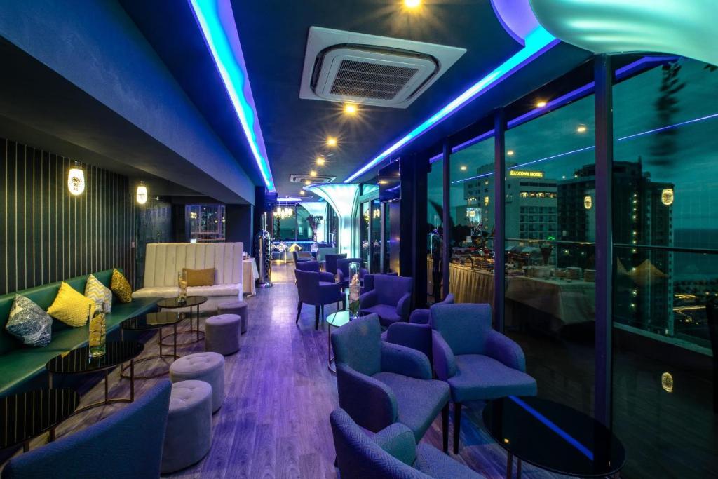 A neon-lit lounge with a bar, armchairs, and city-facing windows.