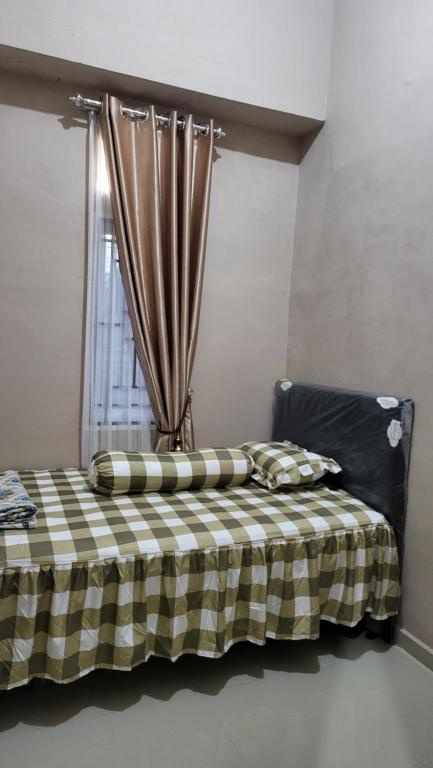 a bed with a checkered blanket and a window at HomeStay Pandan Baru in Halangan