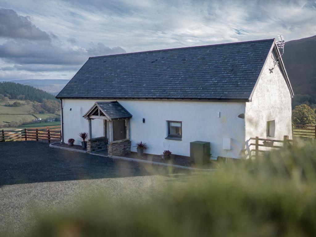 une petite maison blanche avec un toit noir dans l'établissement Tyn Llwyn Barn, à Corwen