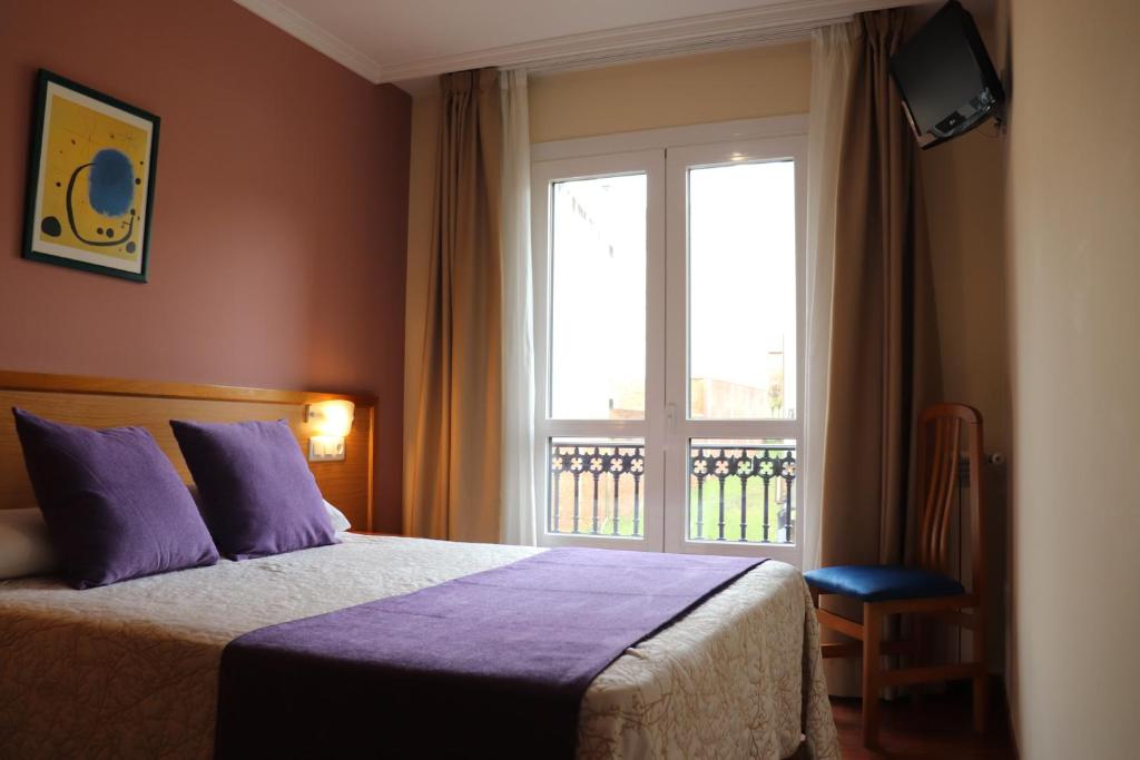 Un dormitorio con una cama con almohadas moradas y una ventana en PENSIÓN RÚA, en Arzúa