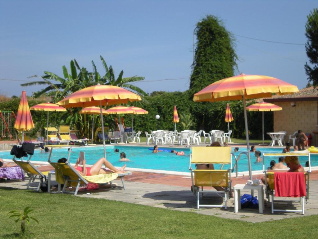 una piscina con gente sentada en sillas de césped y sombrillas en Villaggio Artemide, en Giardini Naxos