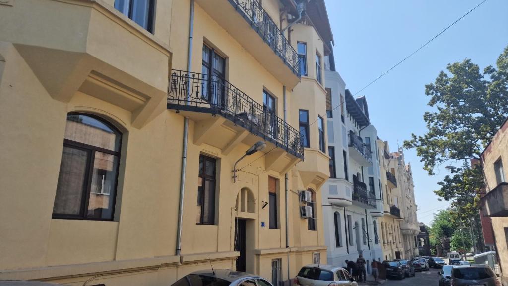 un edificio amarillo con balcones y coches aparcados en una calle en UVS Central Luxury Apartment en Oradea