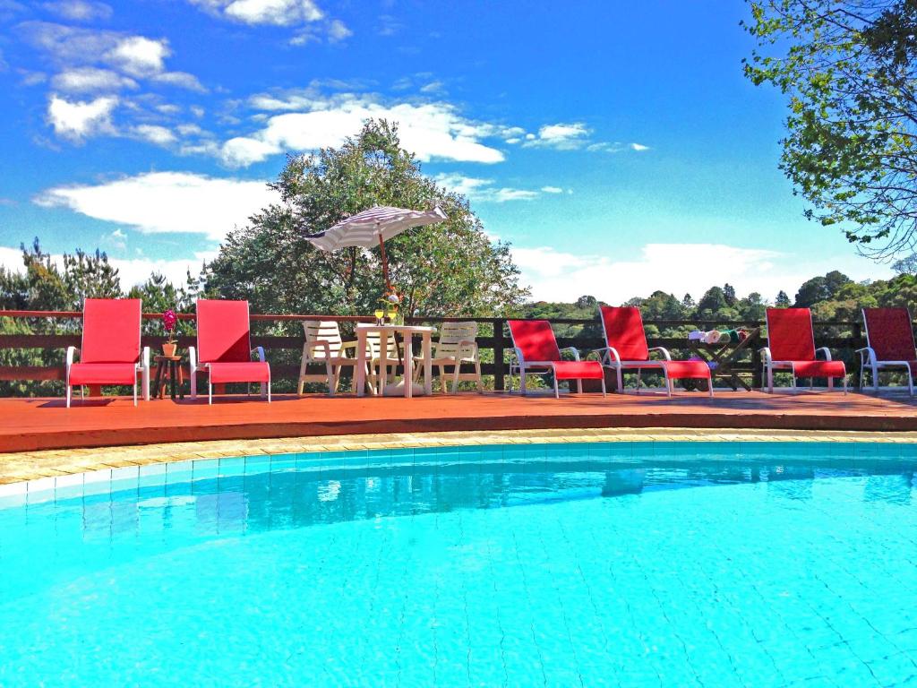 a pool with chairs and a table with an umbrella at Hospedagem Spa da Alma in Monte Verde