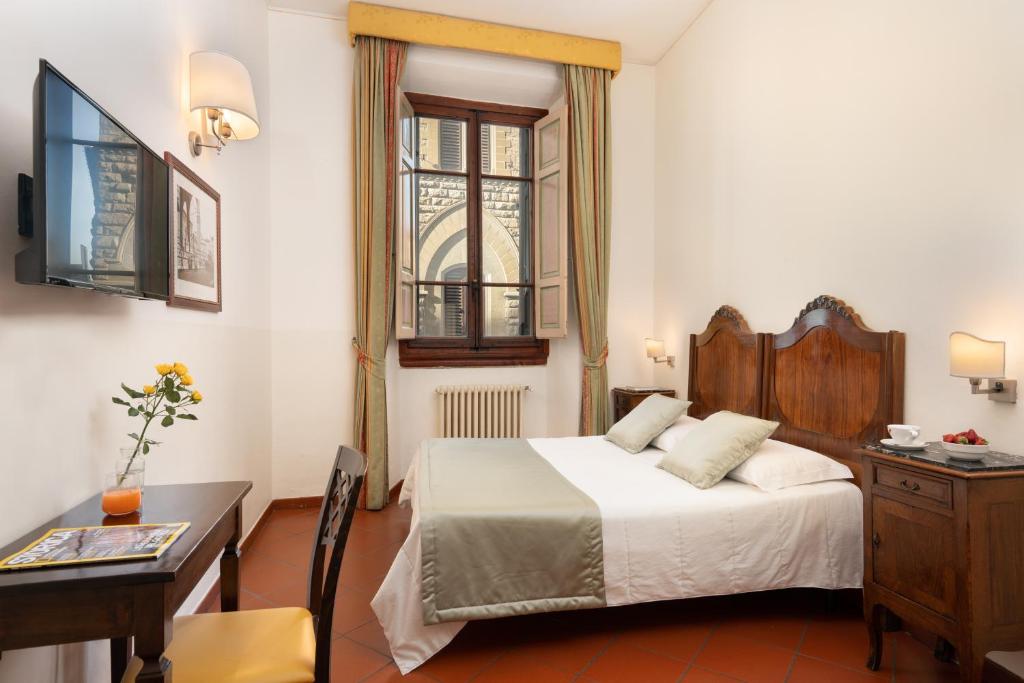 una camera da letto con un letto, una scrivania e una finestra di Hotel Cimabue a Firenze