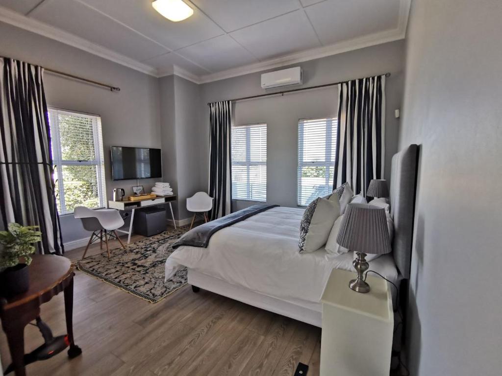 a bedroom with a bed and a desk and windows at Huis van Brood Guesthouse in Malmesbury