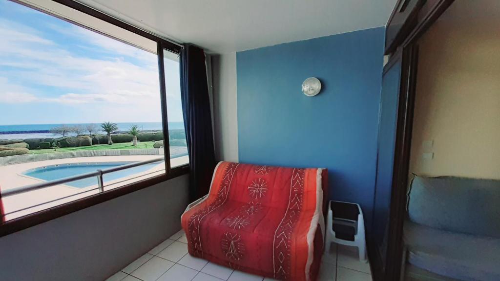 Cette chambre dispose d'un fauteuil rouge et d'une grande fenêtre. dans l'établissement RIVAGES DE ROCHELONGUE Joli T2 piscine vue mer Rochelongue Cap d'Agde, au Cap d'Agde