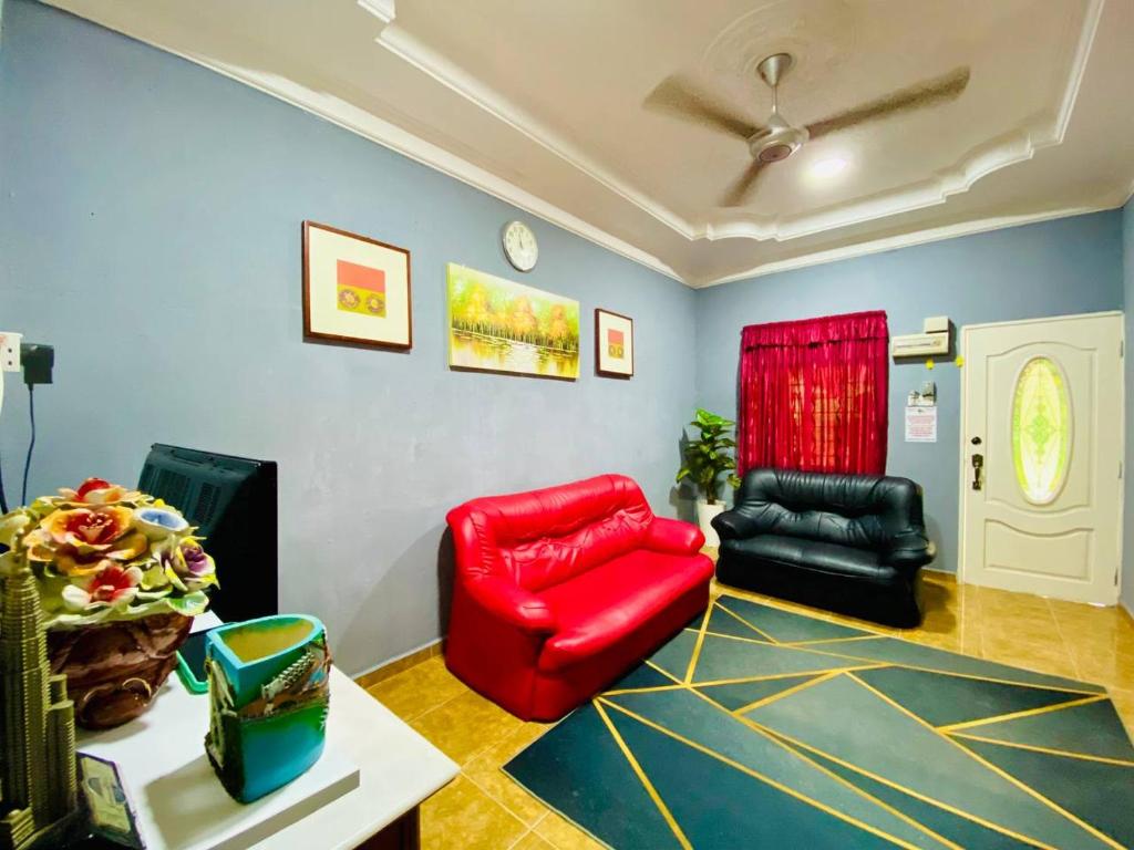 uma sala de estar com duas cadeiras e um sofá vermelho em NABILA HOMESTAY em Pantai Cenang