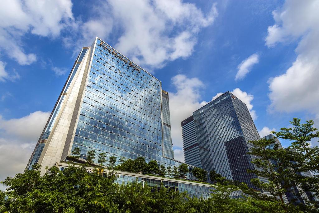 two tall glass buildings with trees in front of them at Four Seasons Hotel Shenzhen in Shenzhen