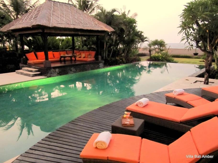 a swimming pool with orange chairs and a gazebo at Bali Amber Villa in Banjar