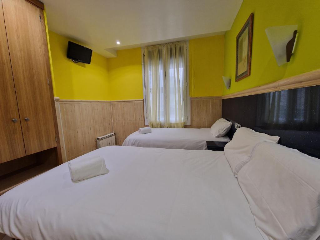 two beds in a hotel room with yellow walls at Pension Izar Bat Guesthouse in San Sebastián