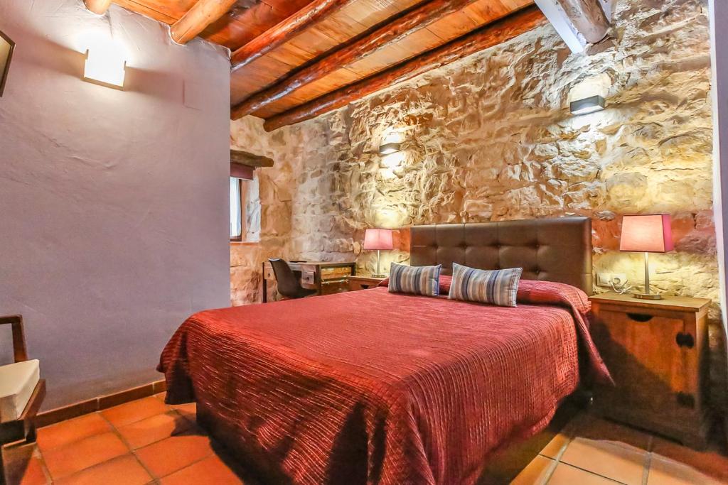 a bedroom with a red bed in a stone wall at Fonda La Grancha in La Fresneda
