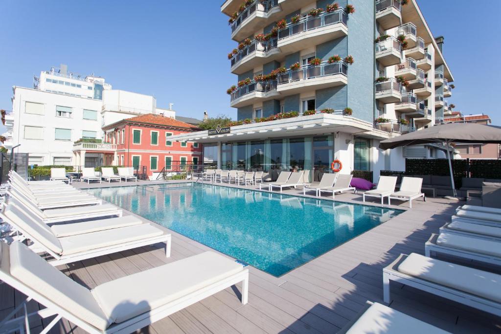 a swimming pool with lounge chairs and a building at Hotel Adlon in Lido di Jesolo