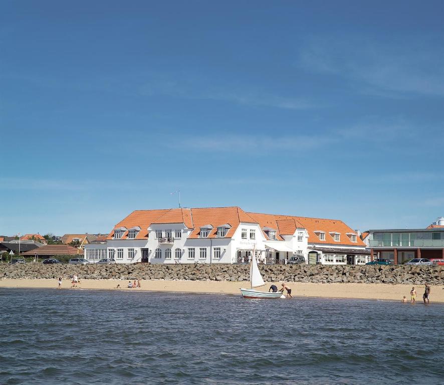 a boat in the water near a beach with houses at Hjerting Badehotel in Esbjerg