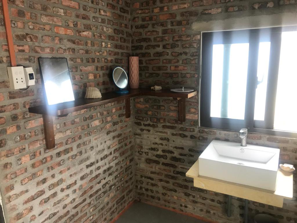 a bathroom with a white sink and a brick wall at You retreat in Quy Thượng