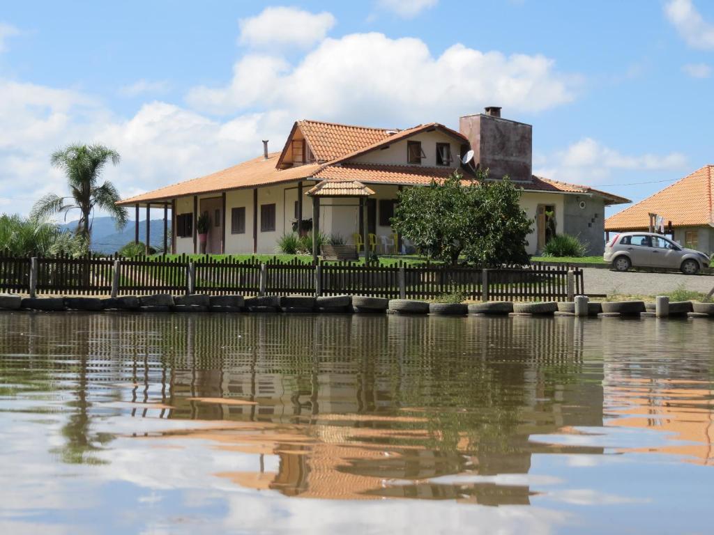 a house with a fence next to a body of water at Pousada Pica Pau in Urubici