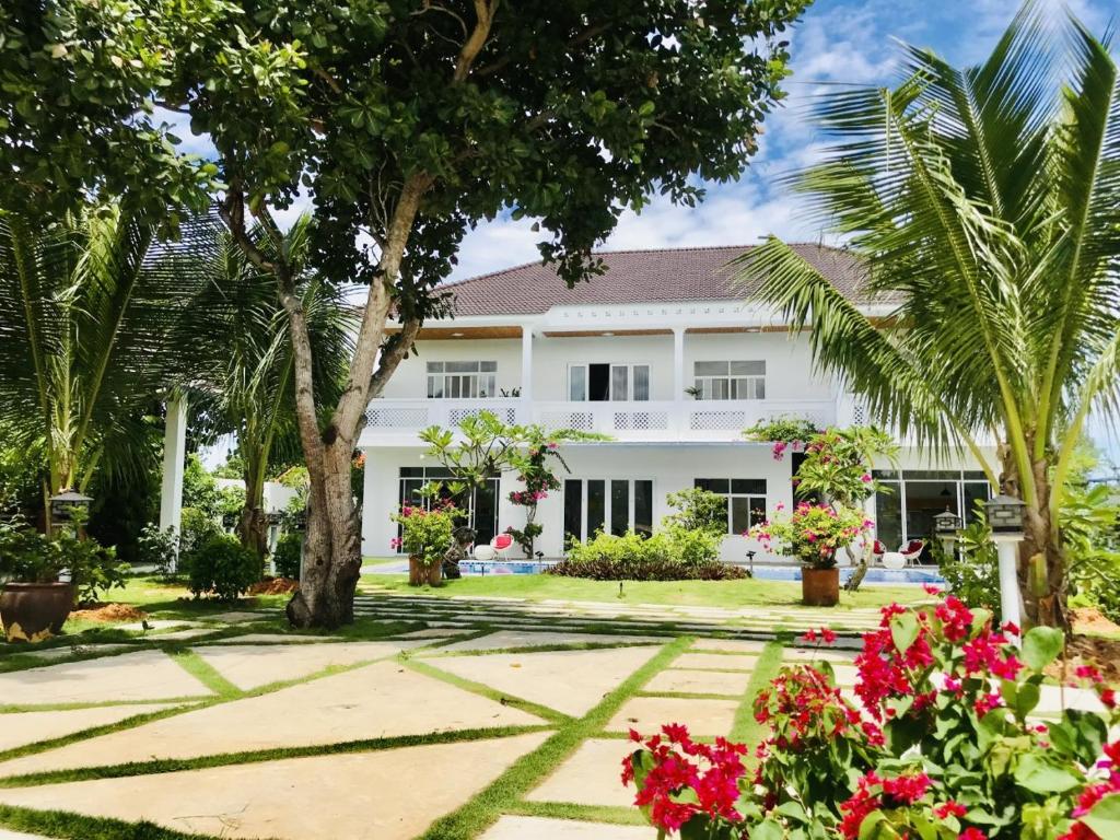 a white house with palm trees and flowers at Casa Vi Mia in Ấp Thiện Sơn